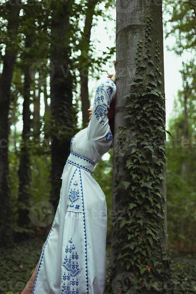 Nahaufnahme einer Frau in besticktem Kleid, die sich an ein Baumstamm-Konzeptfoto lehnt foto