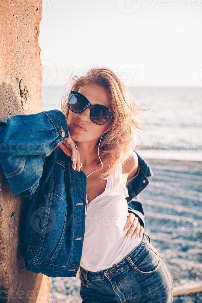 Outdoor-Modeporträt eines stilvollen Mädchens mit Jeansjacke am Strand. foto