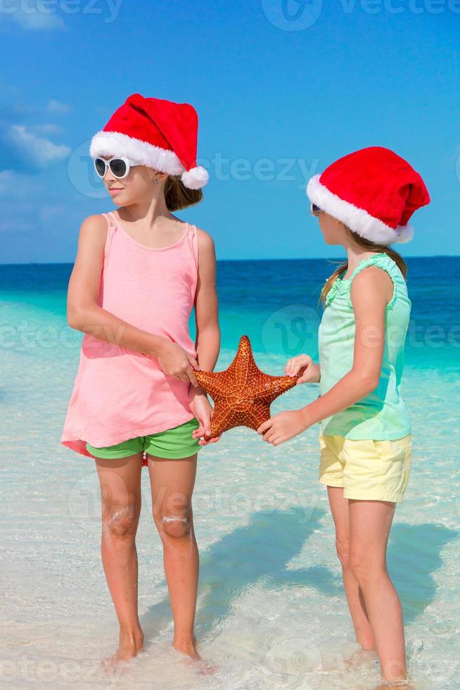 entzückende kleine mädchen im weihnachtsstrandurlaub. Kinder mit Seestern Hintergrund der blaue Himmel und das türkisfarbene Meer foto