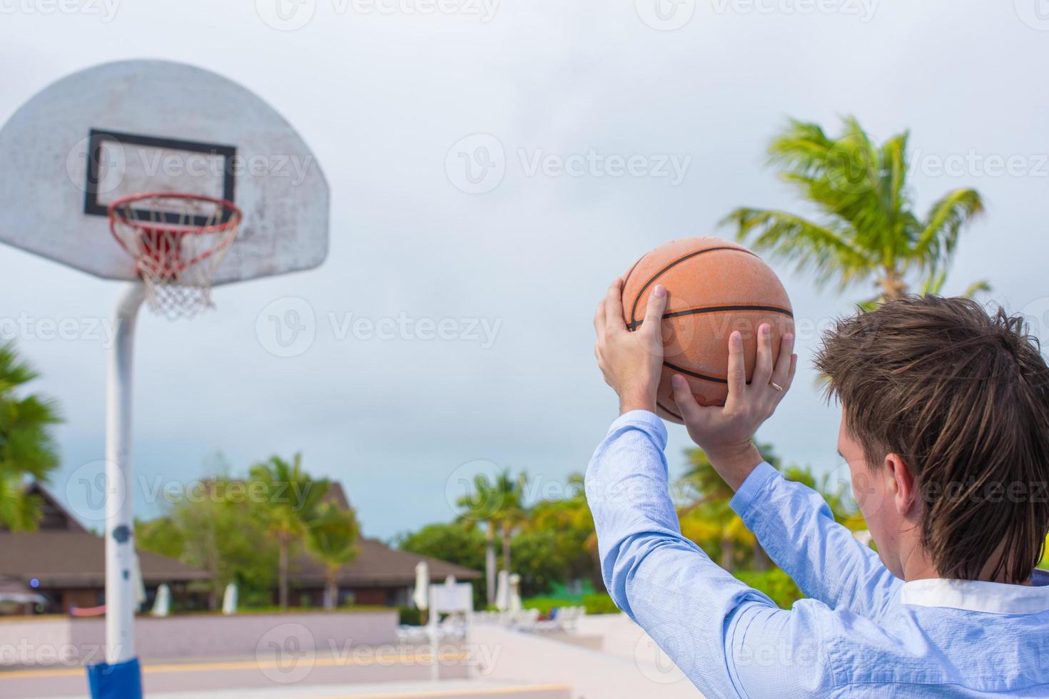 junger Mann, der draußen im exotischen Resort Basketball spielt foto