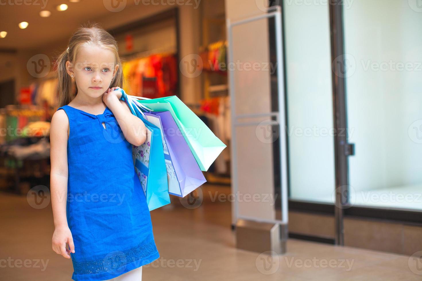 Porträt eines kleinen Modemädchens, das Einkaufstaschen im Einkaufszentrum hält foto