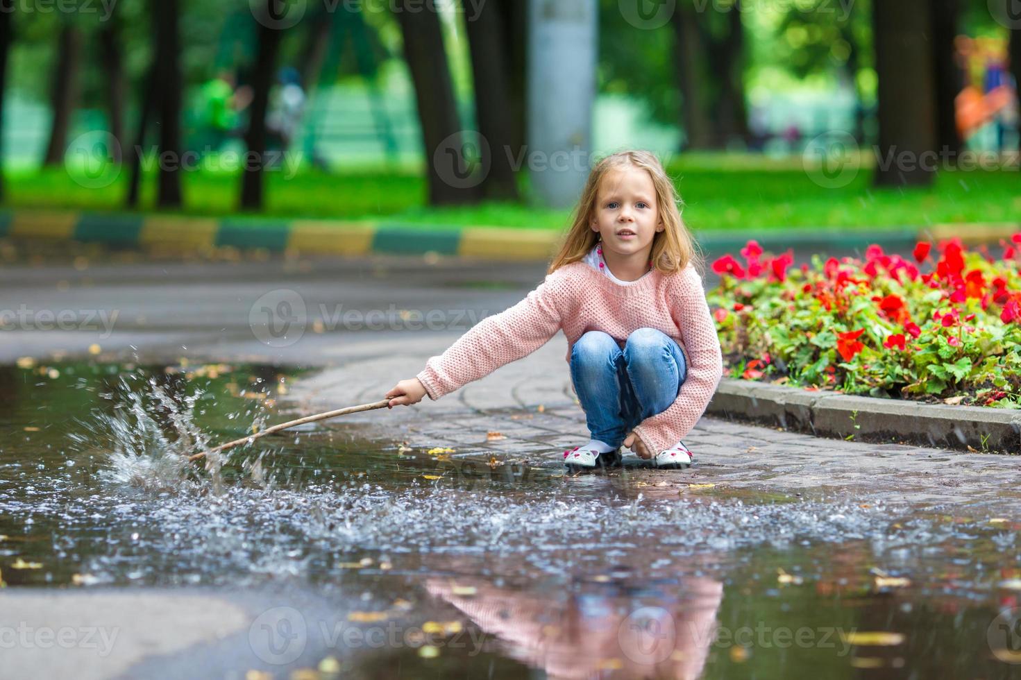 kleines glückliches Mädchen, das sich in einer großen Pfütze im Herbstpark amüsiert foto