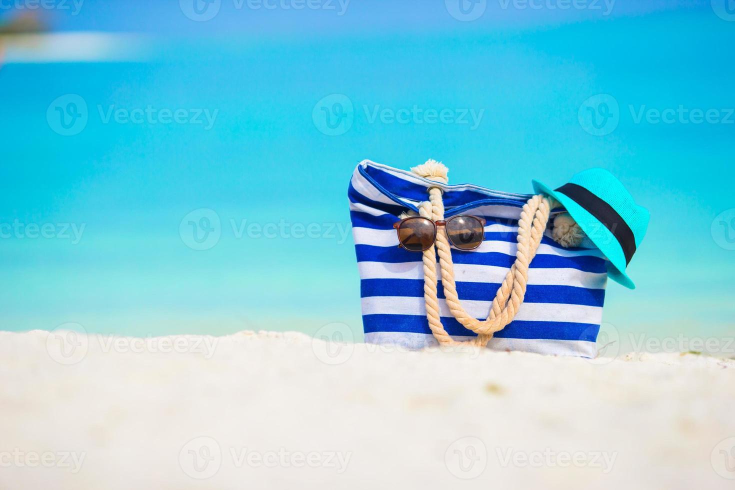 Strandzubehör - blaue Tasche, Strohhut, Sonnenbrille am weißen Strand foto