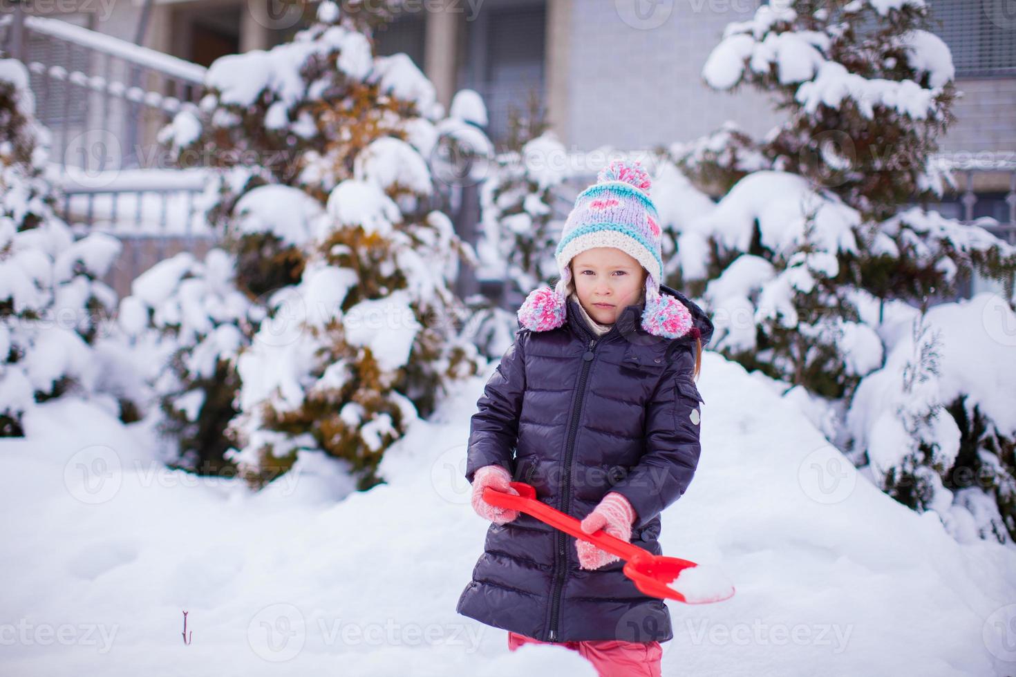 Kleines entzückendes Mädchen spielt am Wintertag mit dem Schneeschaufeln foto