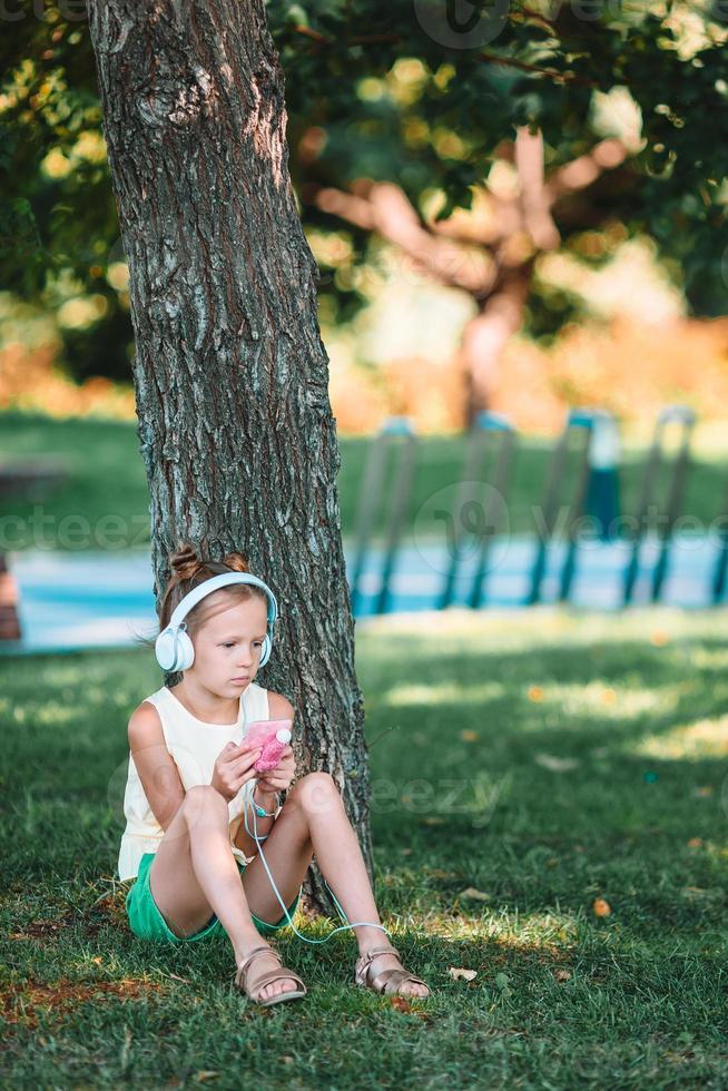 kleines entzückendes mädchen, das musik im park hört foto