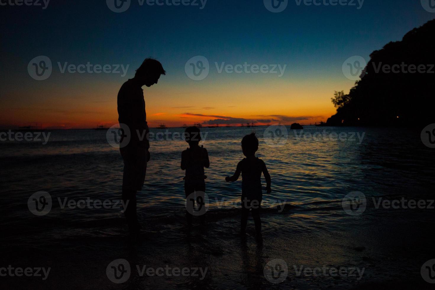 vater und töchter silhouetten im sonnenuntergang am strand auf boracay, philippinen foto