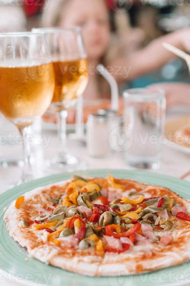 Pizza mit Mozzarella-Käse, Oliven, frischen Tomaten und Pesto-Sauce. am Restauranttisch serviert foto