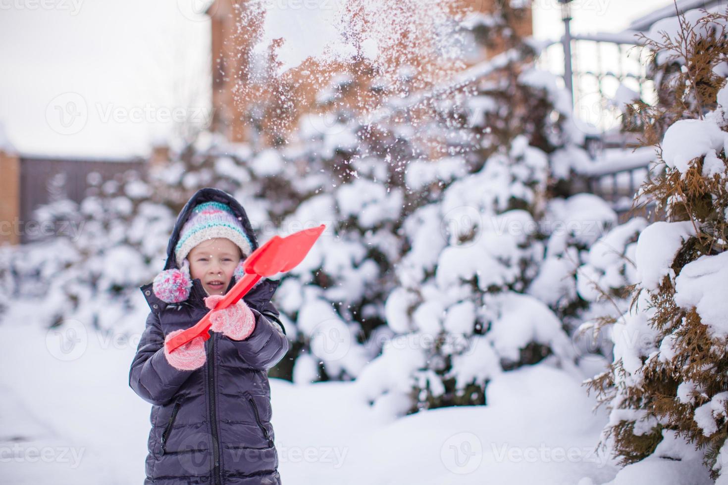 kleines Mädchen spielt mit roter Schaufel im Garten foto