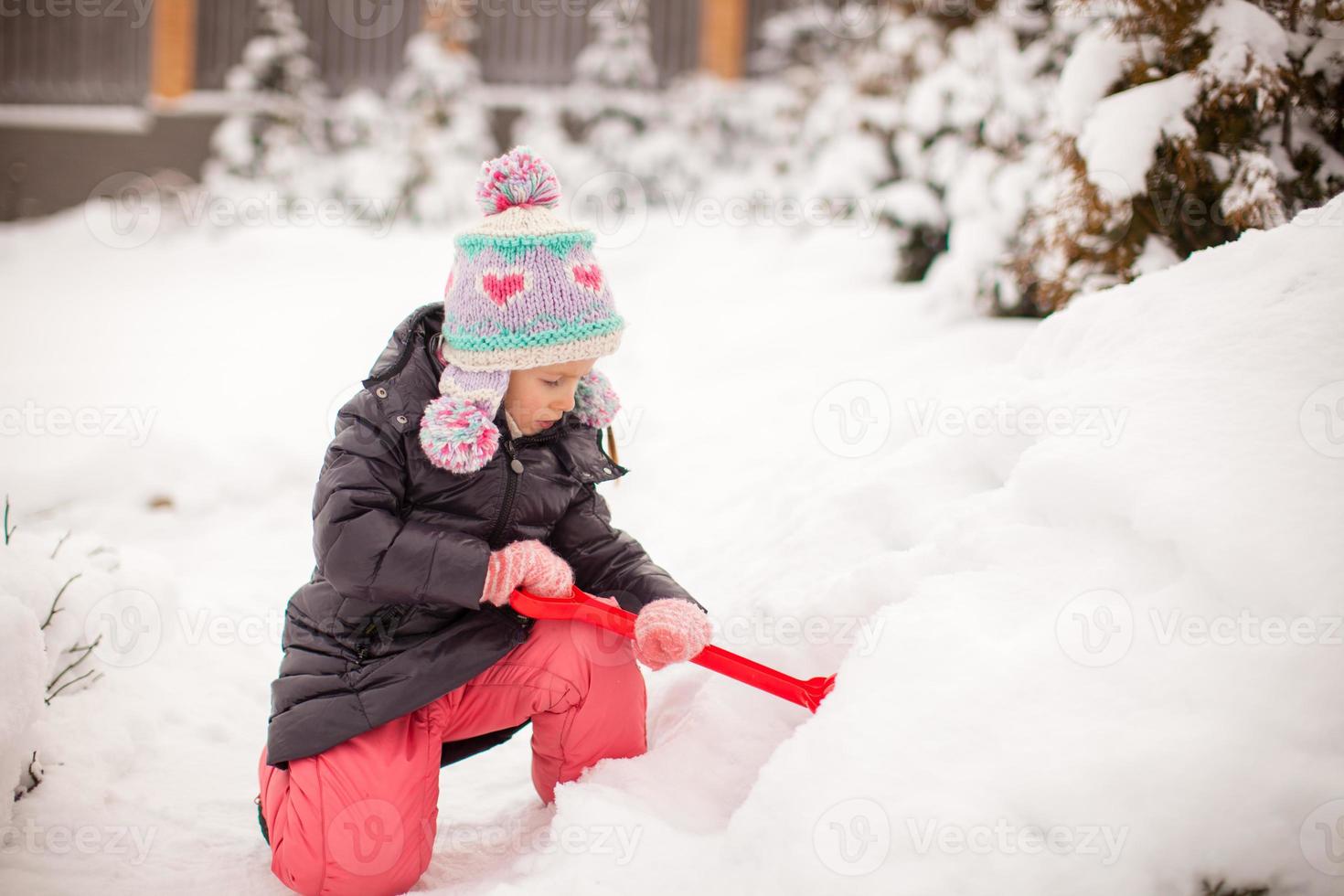 Kleines entzückendes Mädchen spielt an einem Wintertag mit Schneeschaufeln foto