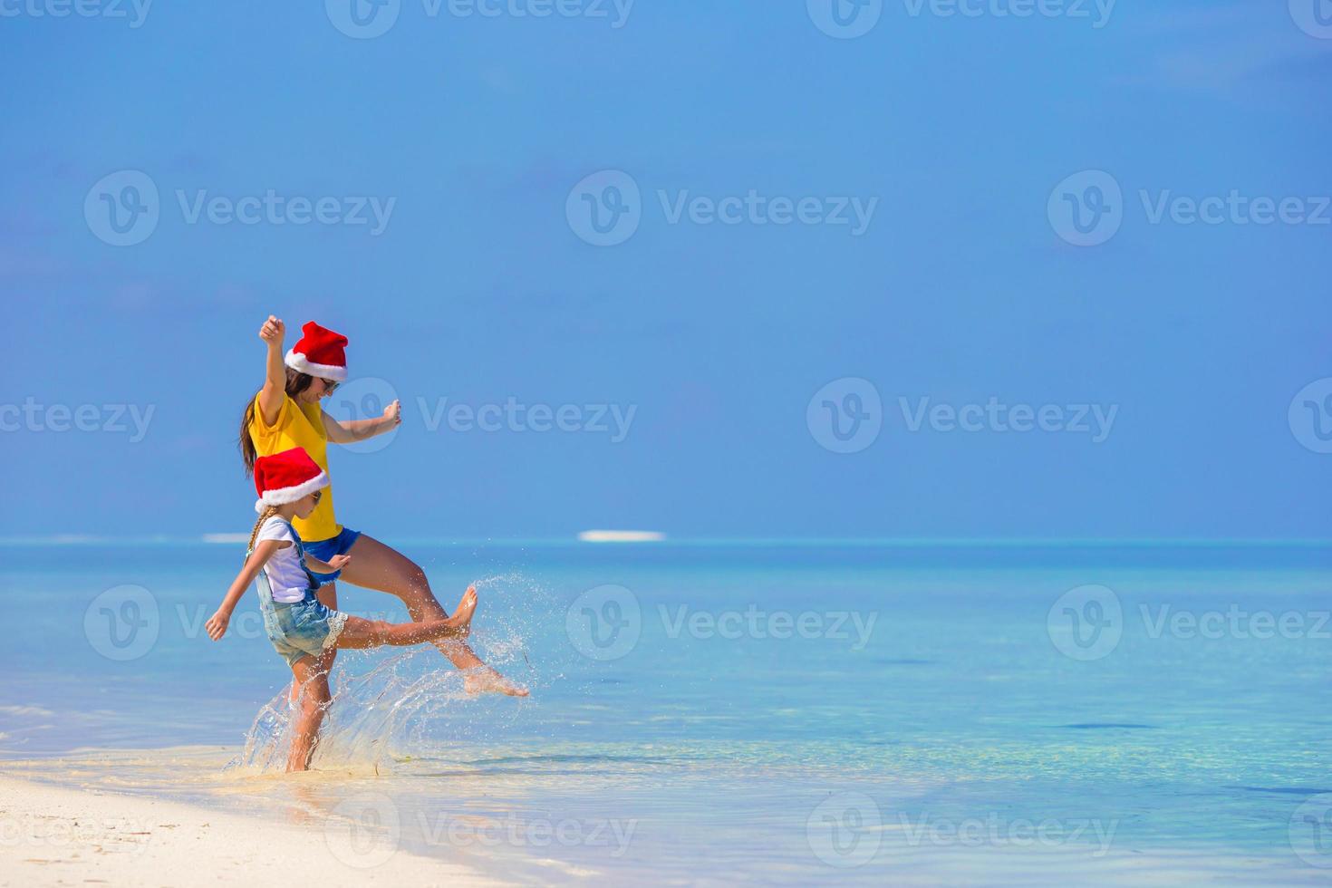 kleines Mädchen und junge Mutter in Weihnachtsmütze während des Strandurlaubs foto