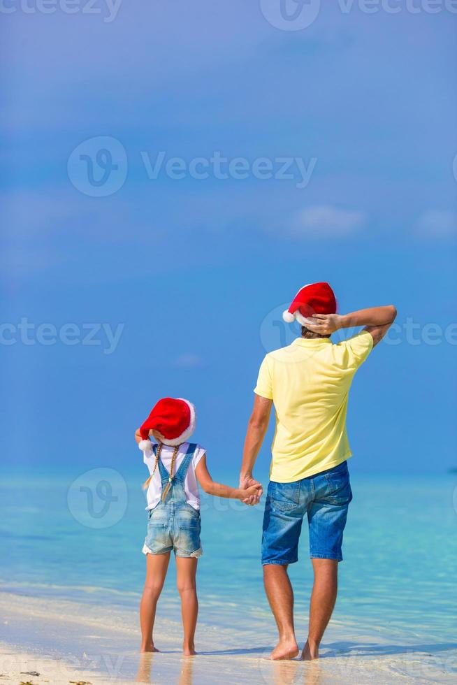 kleines mädchen und glücklicher vater in weihnachtsmütze während des strandurlaubs foto