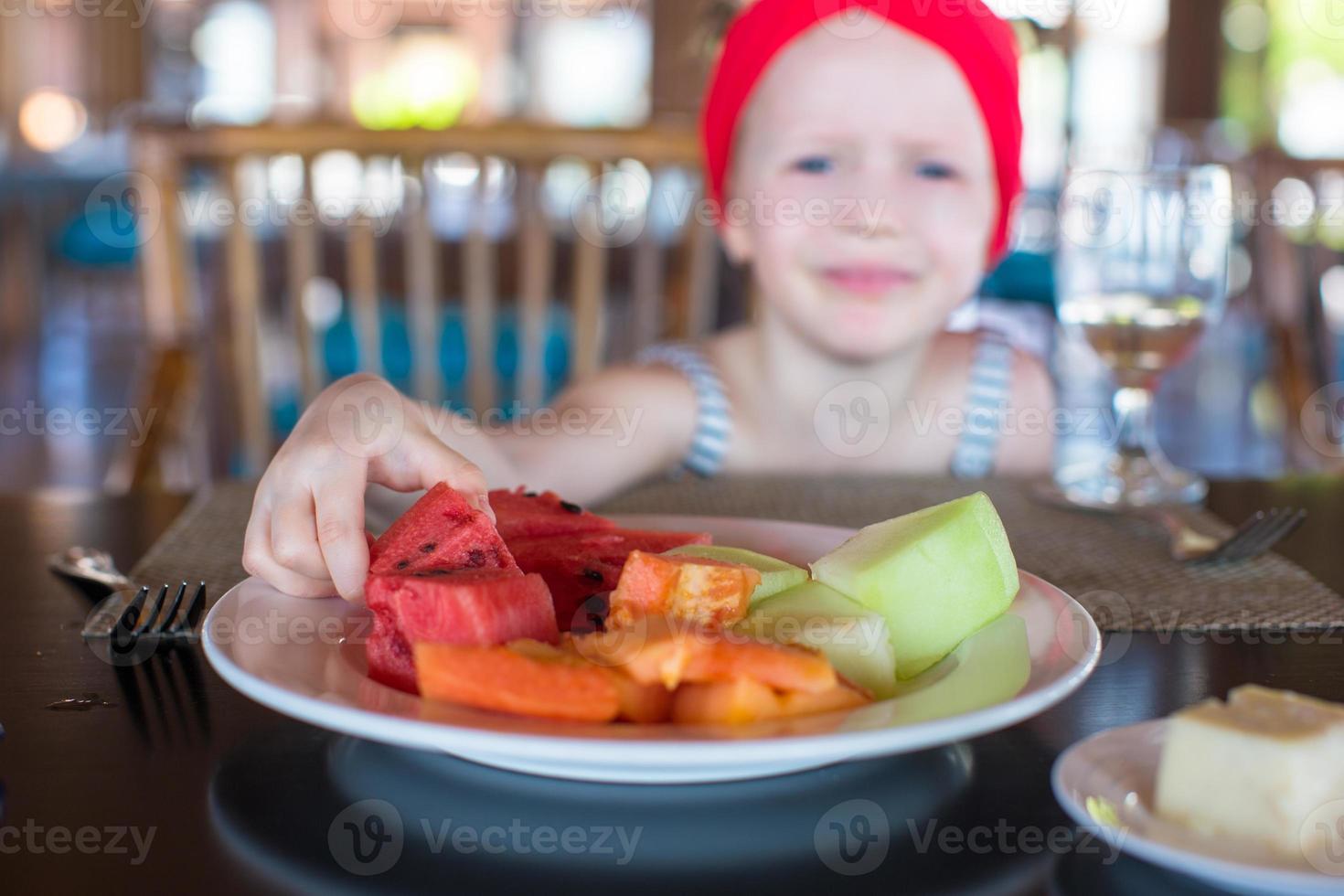 entzückendes kleines Mädchen, das im Café im Freien frühstückt foto