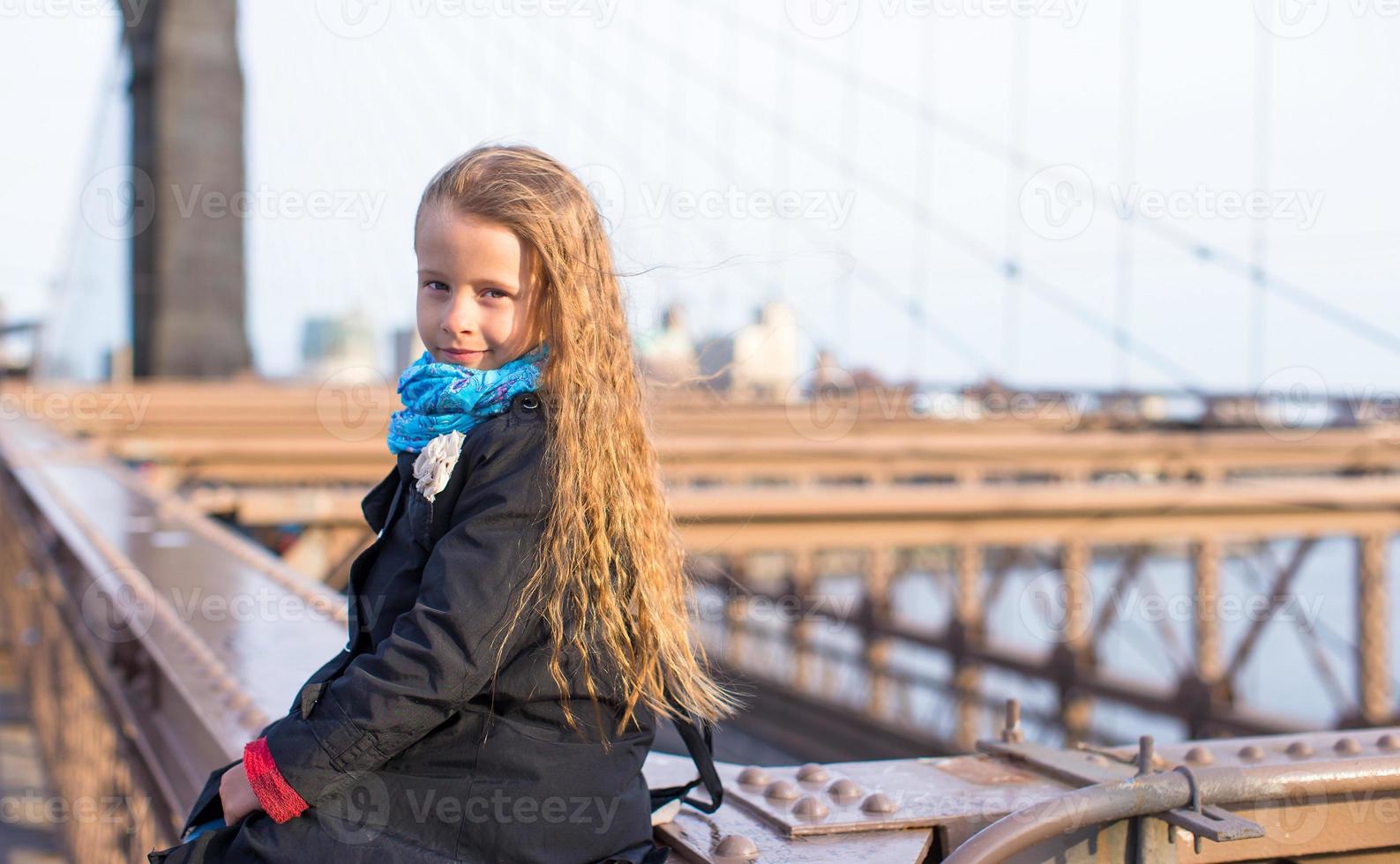 entzückendes kleines Mädchen, das an der Brooklyn Bridge sitzt foto