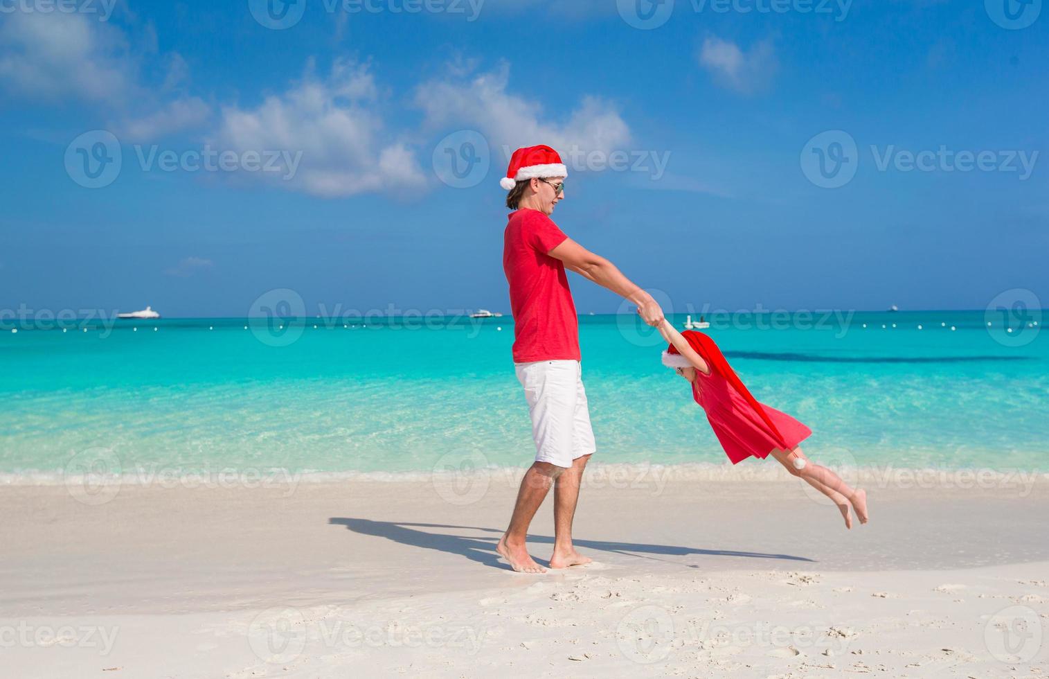 Kleines Mädchen und glücklicher Vater in Weihnachtsmütze haben Spaß am tropischen Strand foto