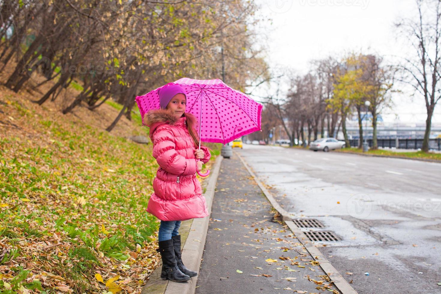 Kleines Mädchen, das am regnerischen Herbsttag unter einem Regenschirm spazieren geht foto