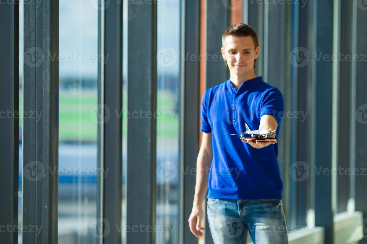 junger kaukasischer mann, der pässe und bordkarte am flughafen in der nähe des fensters hält foto