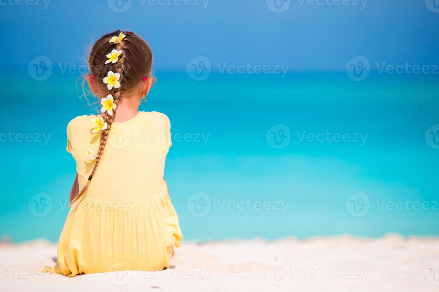 entzückendes kleines Mädchen mit Frangipani-Blüten in der Frisur am Strand foto
