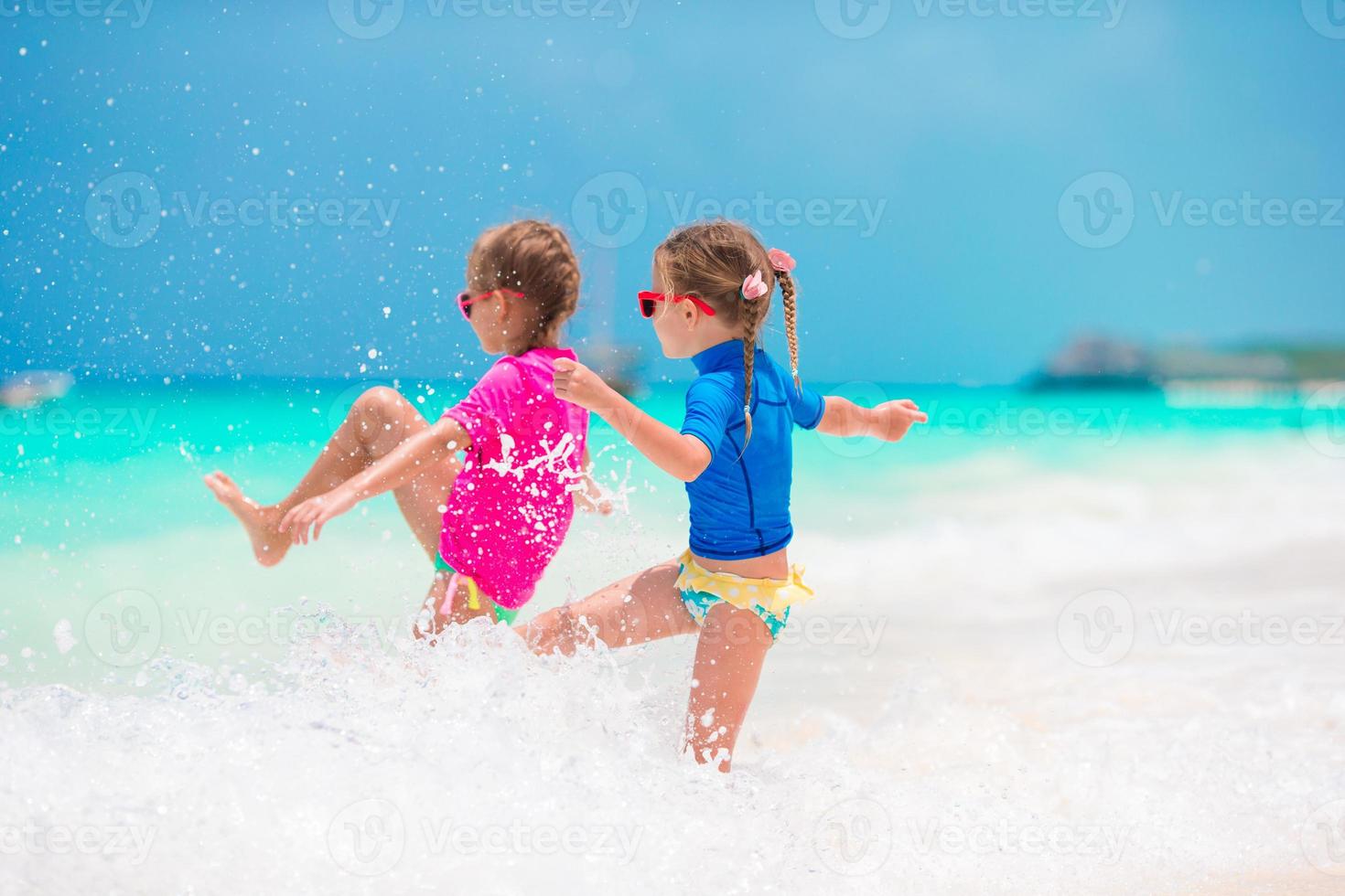 Kleine Mädchen, die sich während der Sommerferien am tropischen Strand amüsieren und zusammen im seichten Wasser spielen foto