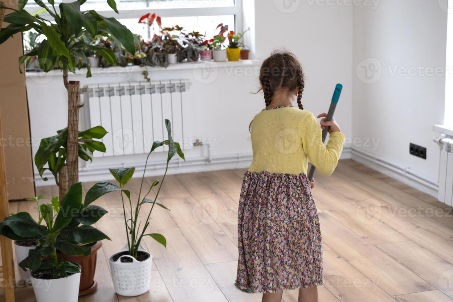 ein Mädchen tanzt mit einem Wischmopp, um den Boden in einem neuen Haus zu reinigen - allgemeine Reinigung in einem leeren Raum, Freude am Bewegen, Hilfe bei der Hausarbeit foto