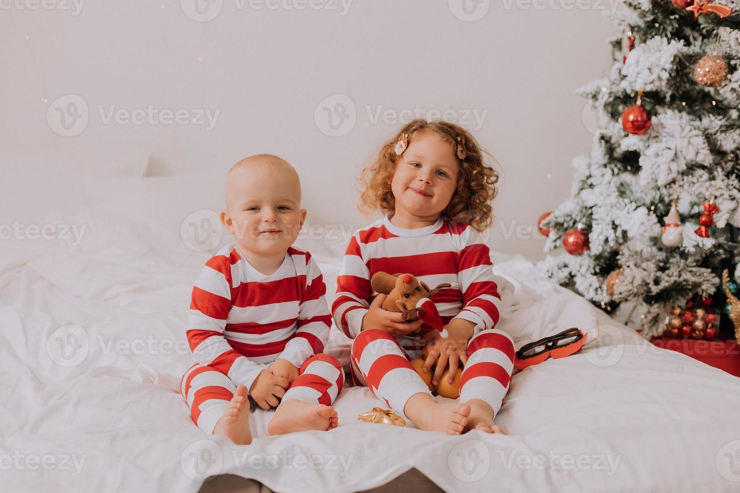 kinder in rot-weißen pyjamas essen weihnachtsbonbons im bett. bruder und schwester, junge und mädchen teilen geschenke. Weihnachtsmorgen. Lebensstil. Platz für Text. hochwertiges Foto