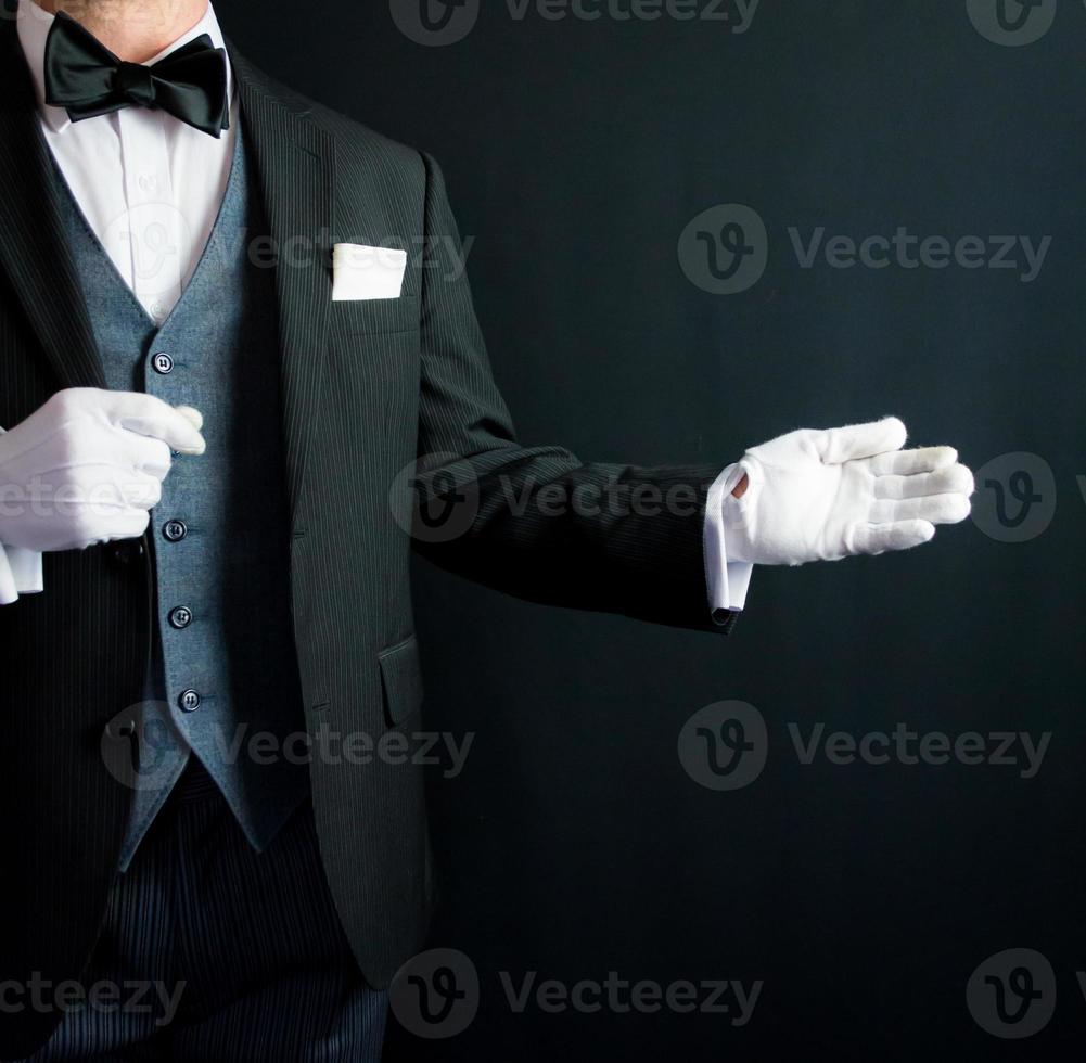 Porträt des Butlers mit einladender Geste im formellen Anzug und weißen Handschuhen. Dienstleistungsgewerbe und professionelle Höflichkeit. foto