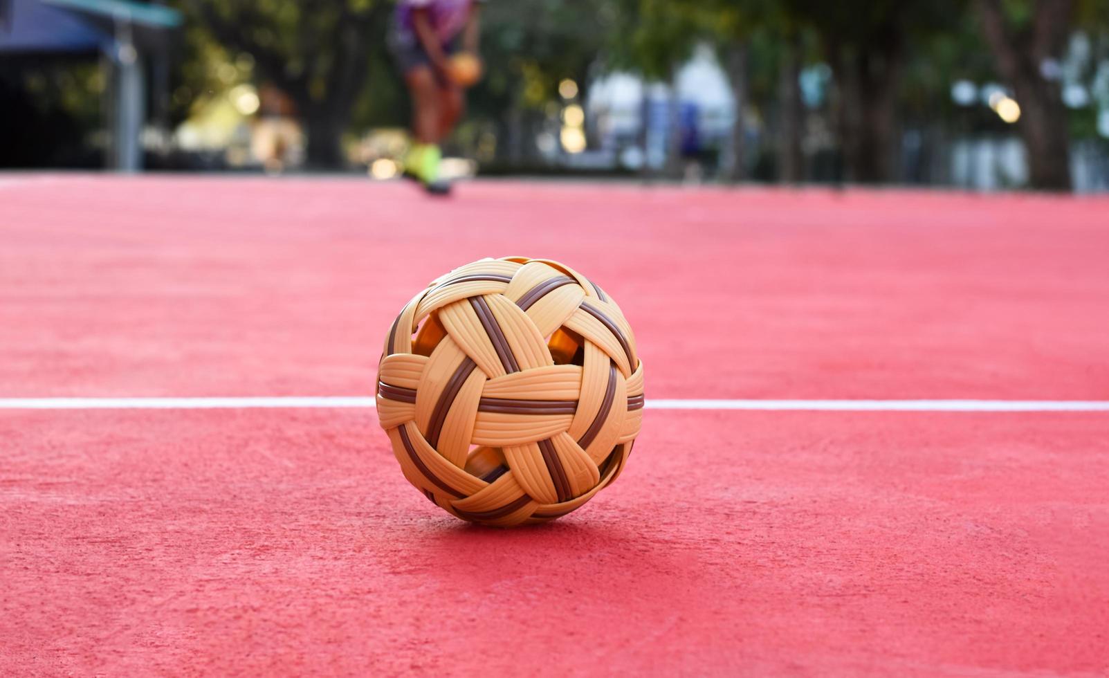 sepak takraw ball auf rotem boden des außenplatzes, unscharfer hintergrund, freizeitaktivitäten und outdoor-sportarten in südostasiatischen ländern konzept. foto