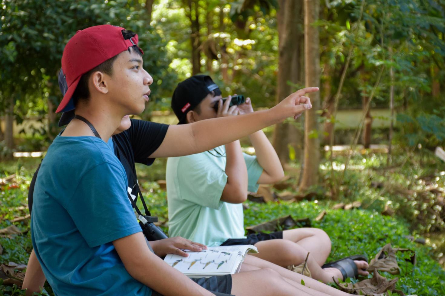 asiatische Jungs benutzen Ferngläser, um während des Sommercamps Vögel im tropischen Wald zu beobachten, eine Idee, um Kreaturen und wild lebende Tiere und Insekten außerhalb des Klassenzimmers zu lernen. foto