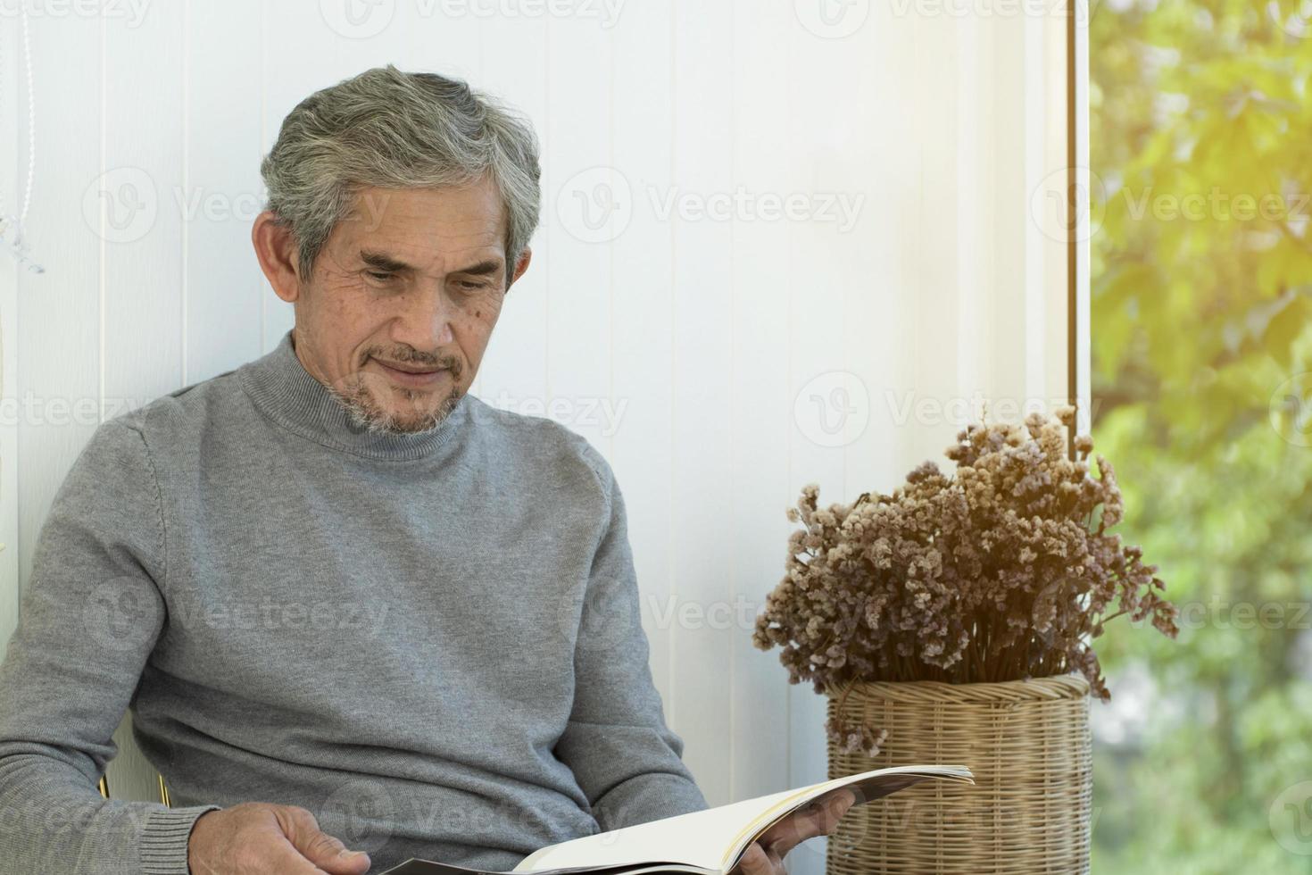 porträt älterer asiatischer mann sitzt morgens in der nähe eines glasfensters, um von zu hause aus zu arbeiten und überprüft sein geschäft auf seinem laptop auf dem tisch ernsthaft, weicher und selektiver fokus. foto