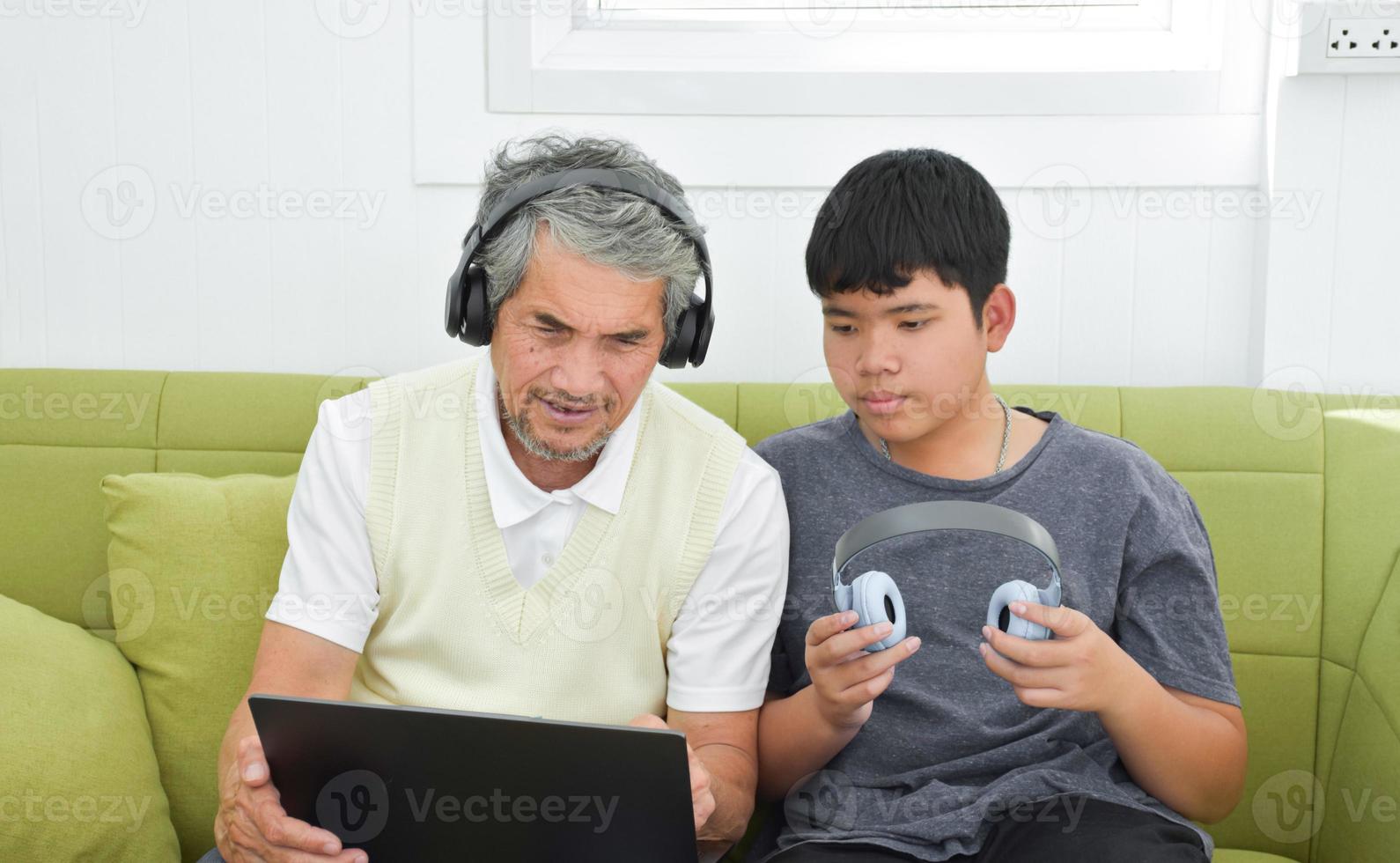 Der asiatische Senior-Opa und sein Sohn verbringen Zeit zusammen zu Hause, um Kopfhörer mit seinem Laptop zu verbinden, um Online-Spiele anzusehen und zu spielen, weicher und selektiver Fokus, Teenager-Konzept aufziehen. foto