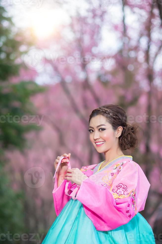 hanbok, das traditionelle koreanische kleid und das schöne asiatische mädchen mit sakura foto