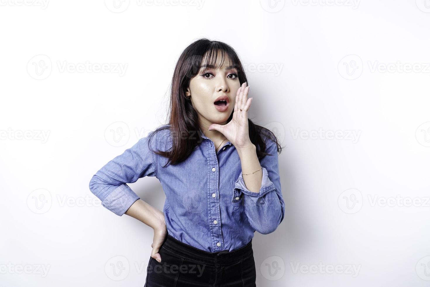 junge schöne frau, die ein blaues hemd trägt, das laut mit einer hand auf ihrem mund schreit und schreit. Kommunikationskonzept. foto