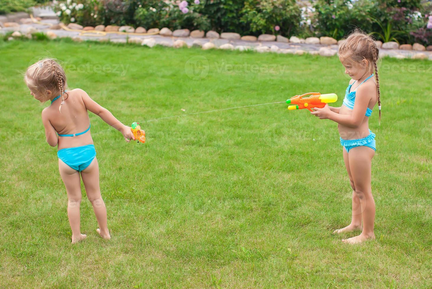 Zwei kleine entzückende Mädchen spielen mit Wasserpistolen im Hof foto
