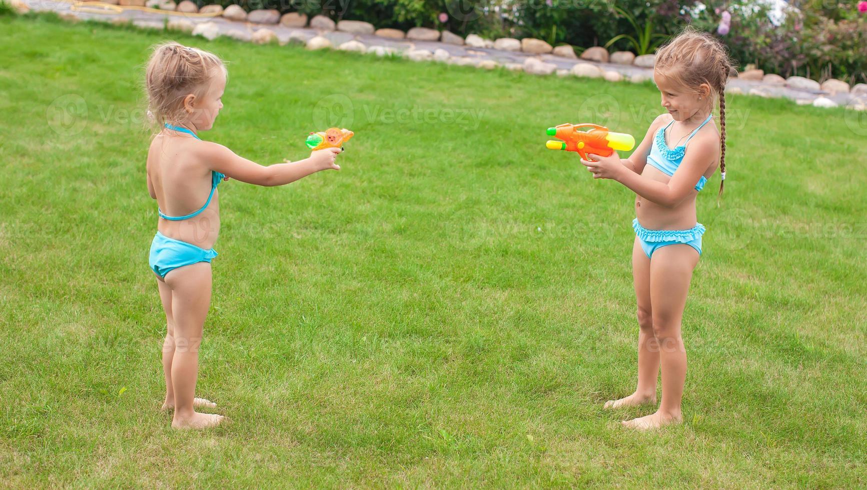 Zwei kleine entzückende Mädchen spielen mit Wasserpistolen im Hof foto