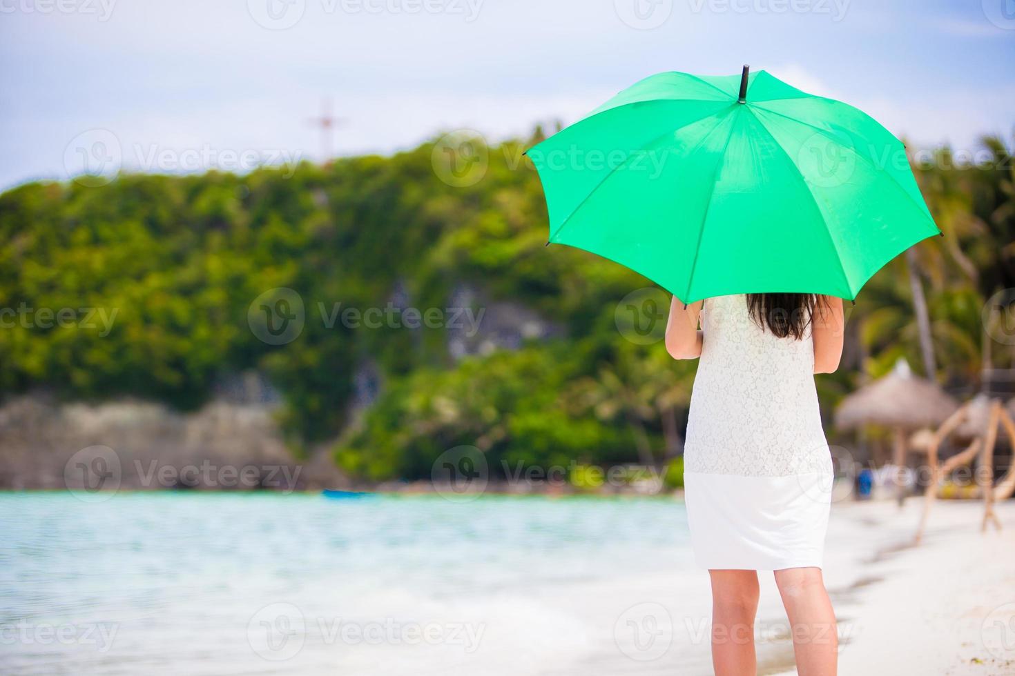 junges Mädchen mit grünem Regenschirm am weißen Strand foto