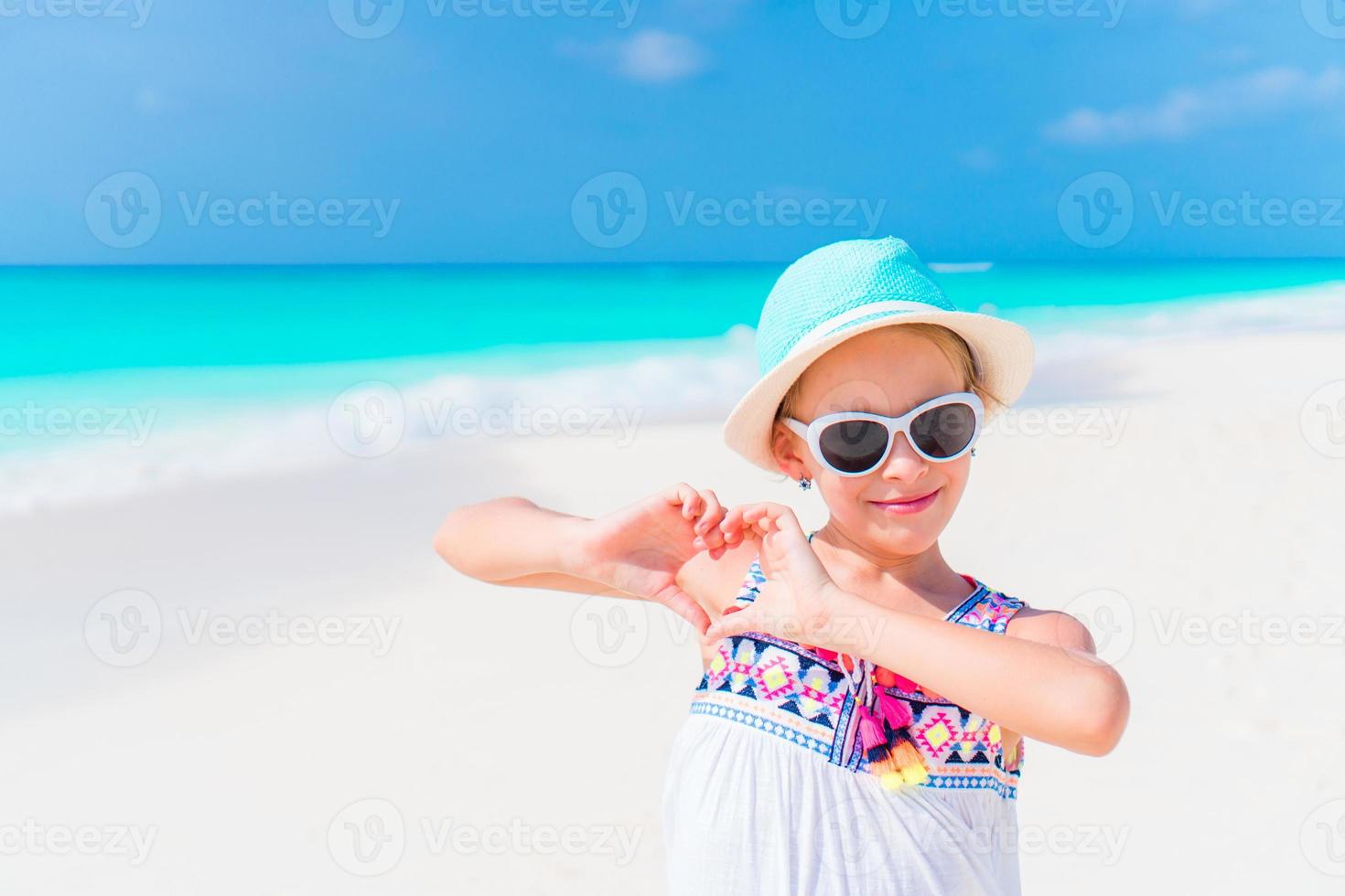 Kleines Mädchen mit Hut, das während des Karibikurlaubs am Strand spazieren geht foto