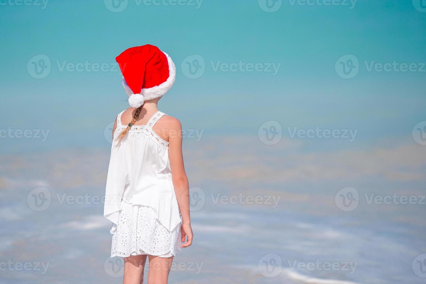 entzückendes kleines Mädchen in der Weihnachtsmütze am tropischen Strand foto