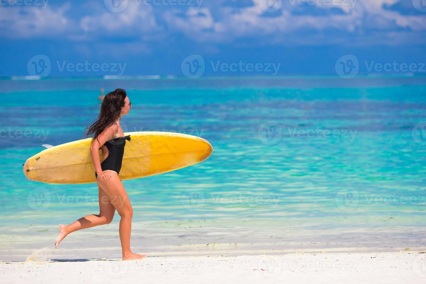 glückliche junge surffrau, die mit einem surfbrett am strand läuft foto