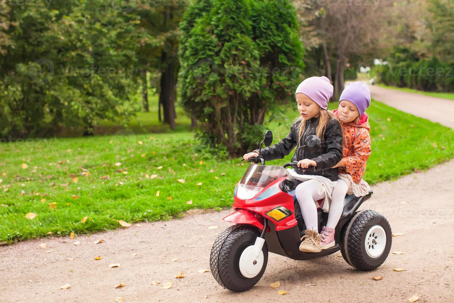 Entzückende kleine Mädchen, die auf dem Kindermotorrad im grünen Park fahren foto