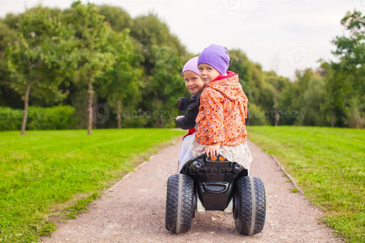 Porträt entzückender kleiner Mädchen, die im grünen Park Motorrad fahren foto