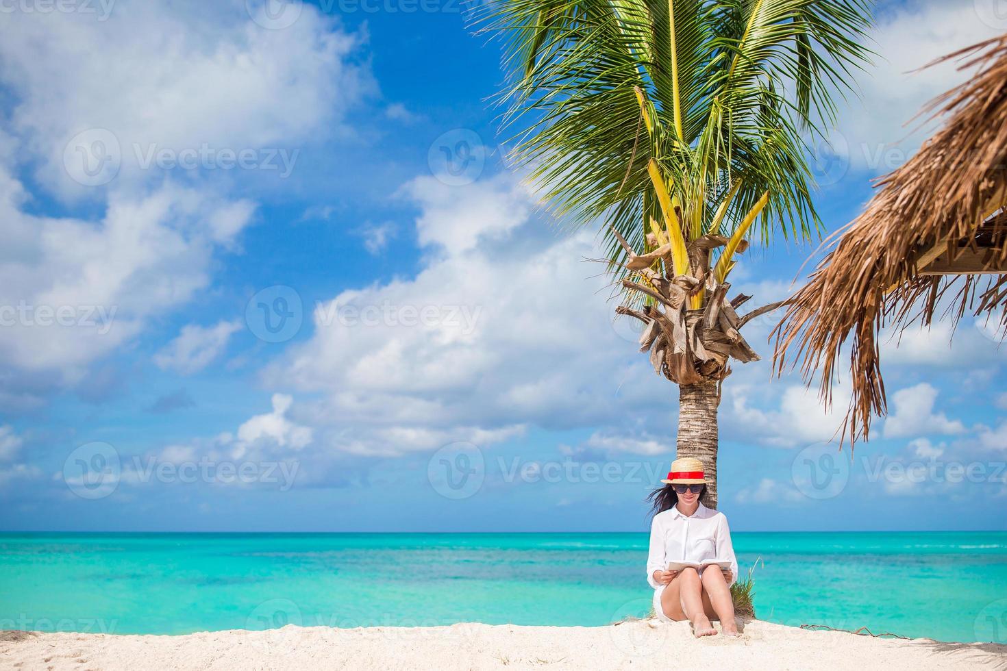 junge Frau liest am tropischen weißen Strand in der Nähe von Palmen foto