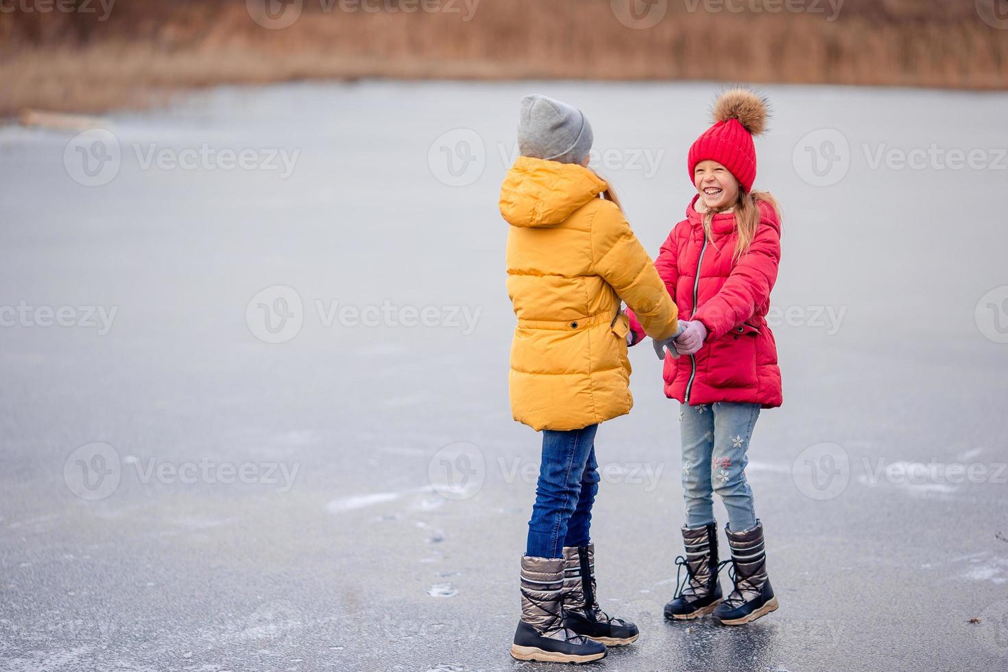 Entzückende kleine Mädchen, die sich gemeinsam auf dem zugefrorenen See amüsieren foto