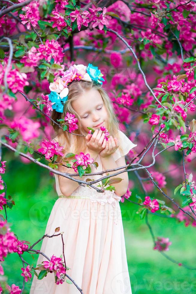 entzückendes kleines Mädchen, das Geruch in einem blühenden Frühlingsgarten genießt foto