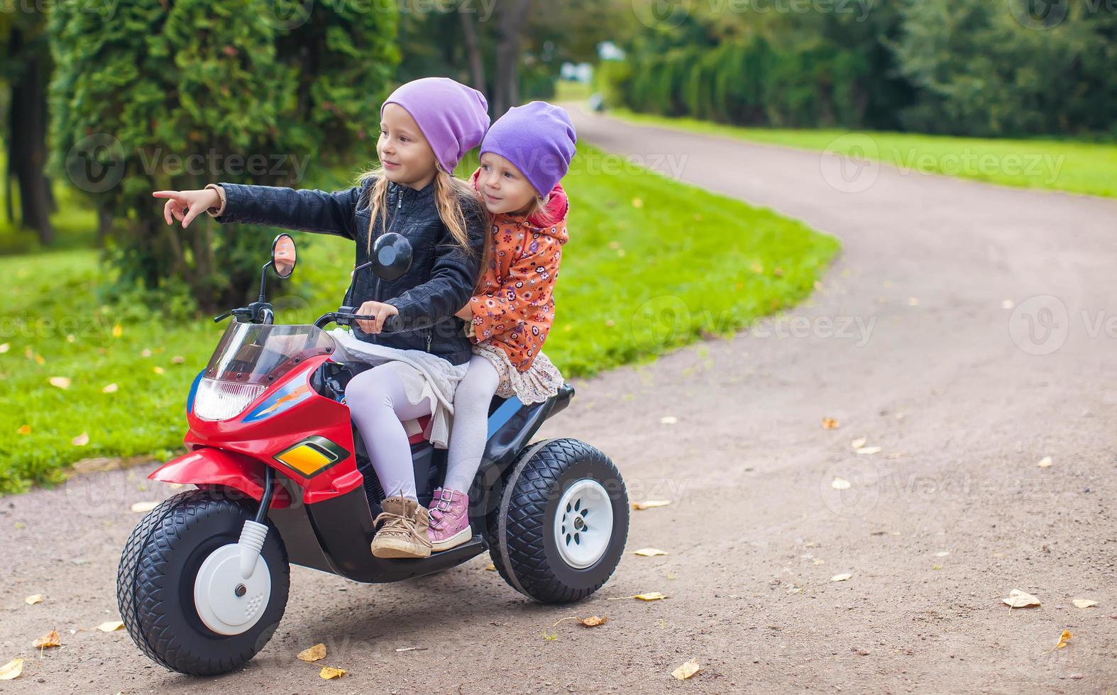 kleine entzückende schwestern, die auf spielzeugmotorrad im grünen park sitzen foto