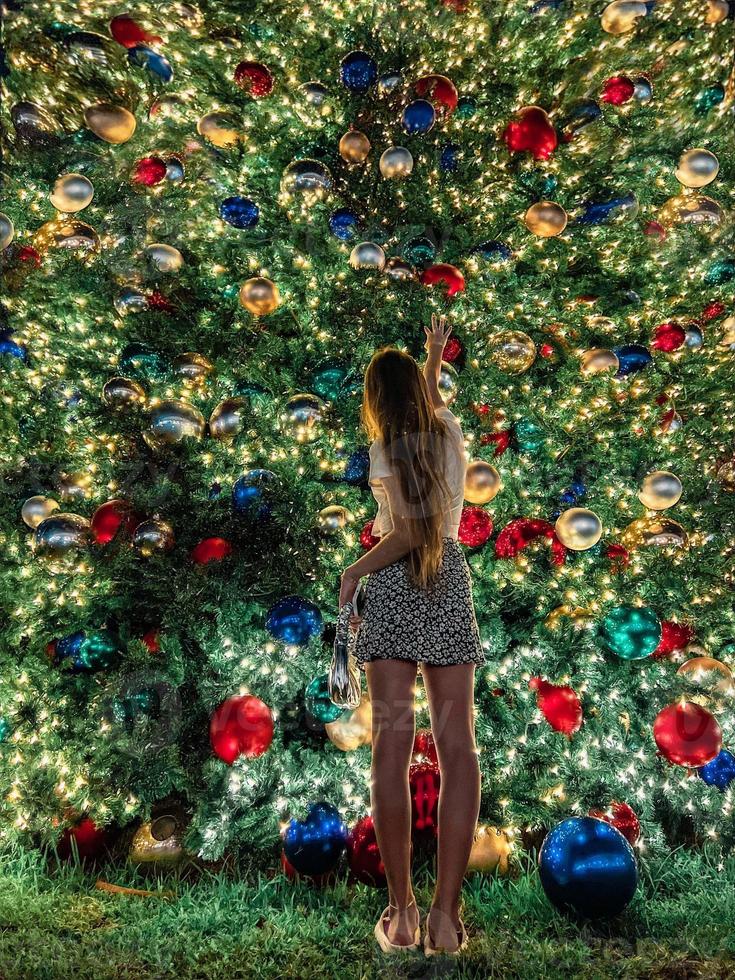 junges Mädchen auf dem Hintergrund des Weihnachtsbaums in Miami. schöner weihnachtsbaum in der beliebten gegend am weihnachtsabend und lichter foto