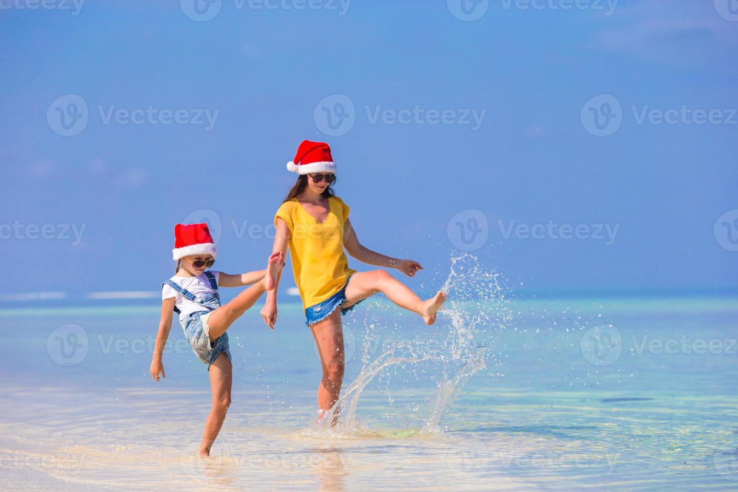 kleines mädchen und junge mutter in weihnachtsmützen während des strandurlaubs foto