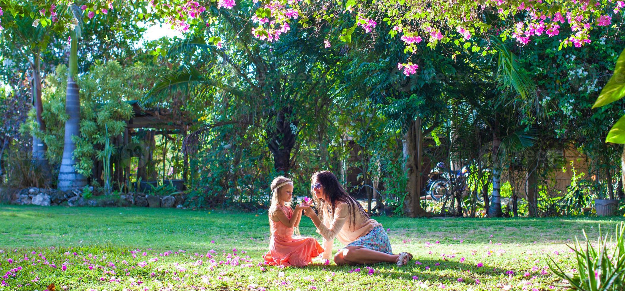 kleines Mädchen mit Mutter sitzt im üppigen Garten und genießt die Sommerruhe foto