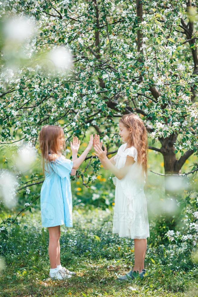 Entzückende kleine Mädchen im blühenden Apfelbaumgarten am Frühlingstag foto