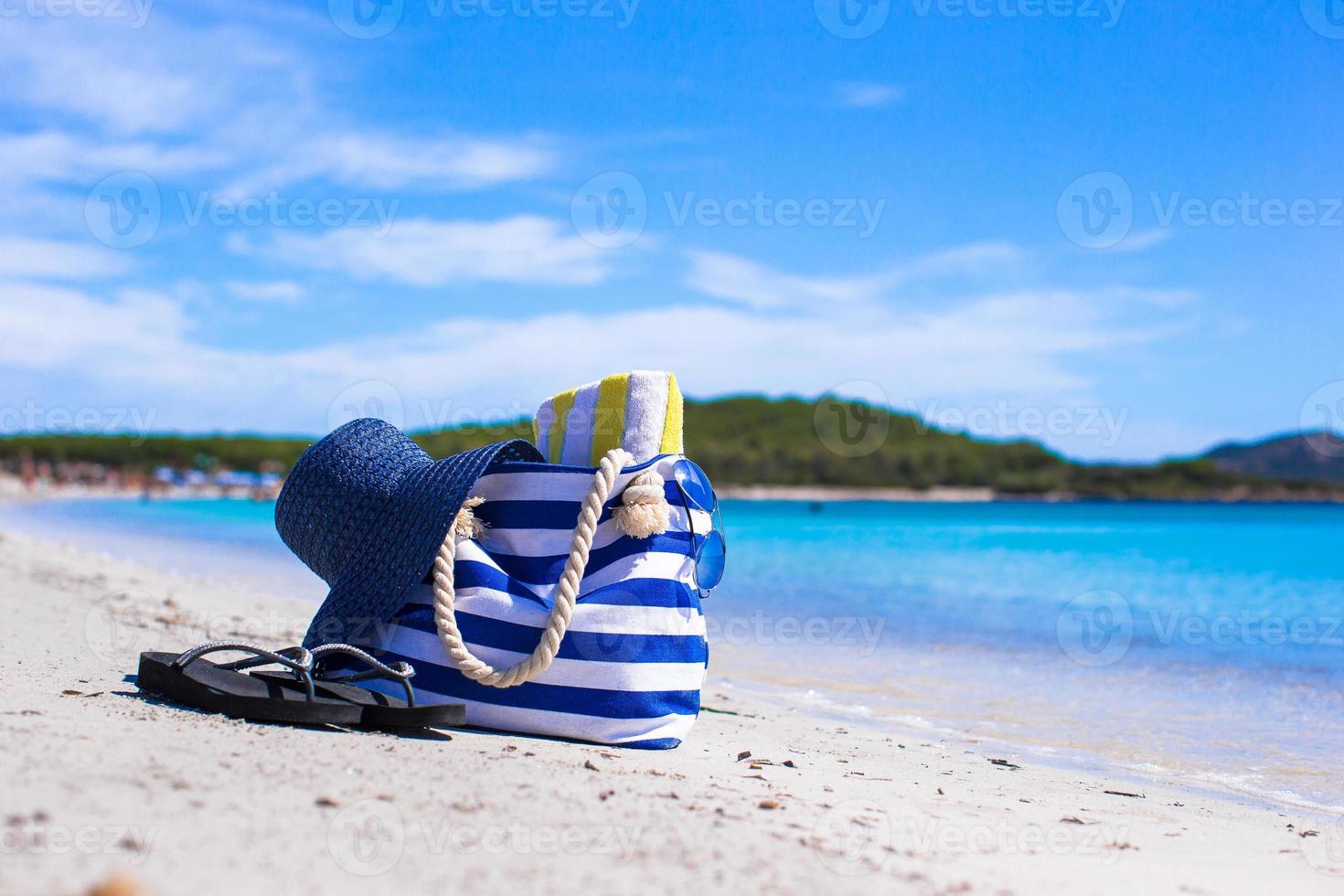 Blaue Tasche, Strohhut, Flip-Flops und Handtuch am weißen tropischen Strand foto