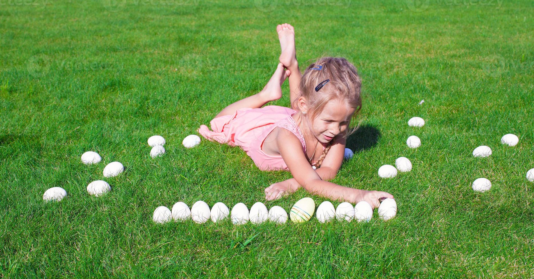 kleines glückliches Mädchen, das mit Ostereiern auf grünem Gras spielt foto