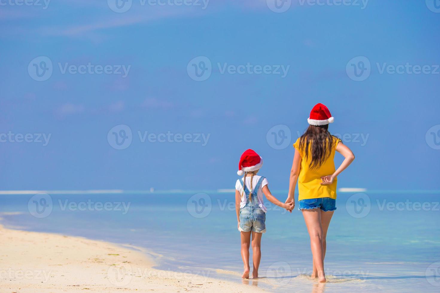 kleines mädchen und junge mutter in weihnachtsmützen während des strandurlaubs foto